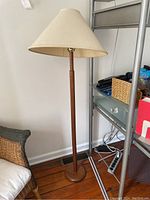 Full view of the wooden floor lamp with beige shade showing its height and style.