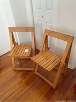 Two wooden folding chairs set up side by side on wood floor, showing slatted seats and backs.