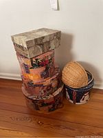 Decorative floral and vintage map patterned hat boxes stacked with a blue Christmas tin can and woven straw hat