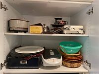 Shelf with multiple kitchenware items including waffle iron, George Foreman grill, small fondue pot, baskets, mixing bowl, and platters.