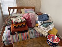 Photo of bed with various blankets, pillows, and folded linens stacked on top