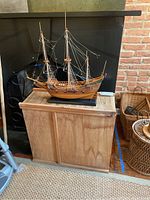 Wooden model ship on top of a wooden storage box near a fireplace.