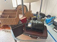 Overview shot showing multiple office supplies on a glass table including wicker baskets, briefcase, bookends, and three-hole punch.