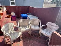 Four white plastic outdoor chairs arranged on a wooden deck outdoors. Chairs show signs of weathering and outdoor use.