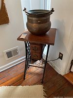 Wooden plant stand with two drawers and black metal Singer treadle legs with large brass bowl on top, shown from a corner angle in room with wooden floor.