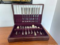 Silverware set inside open wooden storage box showing full set of utensils arranged neatly in fabric compartments.