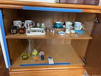 Shelf displaying assorted teacups and saucers, small figurines, and a few glass items