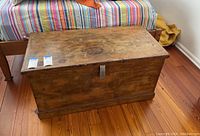 Front view of rectangular wooden trunk showing latch and wooden surface with wear marks.