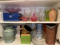 Top shelf showing two pink crystal serving bowls, including one in the Arabia Finland box, various glass vases behind