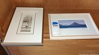 Two framed wall art pieces on wood surface: a black and white architectural drawing and a color landscape titled "Mount Blue" with labels.