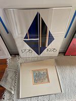 Photo showing the framed geometric art print and the abstract art print laid on a cream carpeted floor with backing protection around the edges.