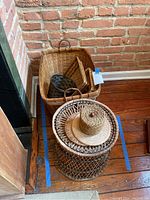 Wicker baskets stacked in corner including cylindrical open lattice basket with woven hat on top, large rectangular basket beneath, and smaller baskets beside