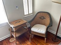 Wicker armchair with beige cushion, curved backrest with black edging and decorative diamond pattern on the back.