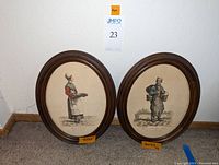 Two oval-wood framed prints showing merchant figures standing against a neutral background, measuring 12x14.5 inches.
