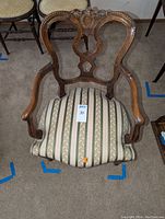 Full view of wooden arm chair showing carved backrest and striped cushioned seat