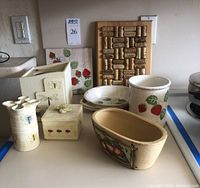 Top view of the full set showing the cork cork board, clay trivet with strawberry design, round roasting/serving dish, vase with butterfly, oval strawberry planter, and other small decorative kitchen items.