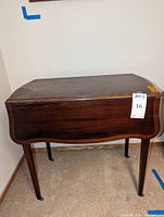 Full view of the drop leaf table showing curved wooden design, tapered legs, and casters.