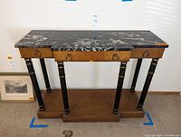 Full view of the Empire style console table showing black marble top, wooden body, columnar legs with gold accents, and plinth base.