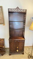 Front view of tall wooden etagere cabinet with open shelves and closed cabinet doors below.