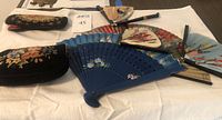 Multiple Asian handheld fans in various sizes and painted designs arranged on a white cloth.