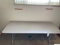 Full view of the 6 foot folding table showing rectangular white top with wear marks and scratches.