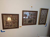 Three framed textile artworks displayed on a wall: two needlepoint samplers on left and center, one lace tatting in a cream frame on right.