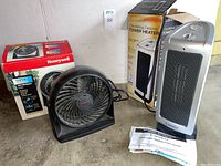 Photo showing Lasko ceramic tower heater, Honeywell high performance fan, their boxes, and manual for the Lasko heater on the floor.
