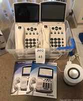 Two Ultratec CapTel 840i phones in a plastic bin along with their setup guides and an additional Logitech small speaker unit.