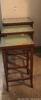 Photo showing stacked vintage nesting tables with brown legs and green painted tops featuring floral and ornamental patterns