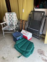 View of lot showing two different outdoor folding chairs, two coolers, small folding table, and chair cushions