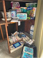 Wide view of wooden shelves holding various assortments of paper towels, toilet paper rolls, napkins, paper plates, cups, and bags.