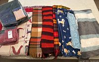 Photo showing new packaging of Ralph Lauren bedding in red and assorted used blankets including plaid, striped, and dog-patterned fleece blankets.