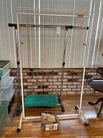 White rolling clothes rack with a top shelf and a green bath rug underneath it. Clothes rack has four caster wheels.