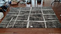 Full view of the rectangular black and grey area rug with white grid stripes on a wooden floor.