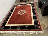 Full view of the red central field with cream medallion and black border with Asian-inspired symbols and fringe on one end.