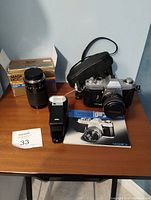Yashica FX-2 camera with lens mounted, Braun 260 BC flash, zoom lens box, and instruction manual on table.