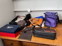 Purple lunch bag, six baseball caps, sports jacket, and various bags on a wooden surface