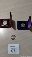 Two commemorative coins in display cases and one encapsulated coin with MaxSold lot number visible.