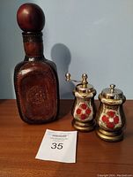 Leather-covered decanter with embossed floral design alongside Italian Florentine salt and pepper grinders with floral patterns.