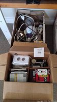 Cardboard boxes containing multiple electrical items including light bulbs, switches, plugs, flashlight, and night light.