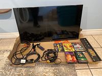 40-inch Roku TV with remote, legs, wall mount bracket, and all cables arranged in front.