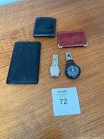 Overview of all items in the lot: three wallets/card holders, silver Seiko quartz watch, black clip pedometer on wooden surface.