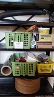 Photo showing shelves with green and yellow plastic baskets containing various hardware and household items such as batteries, door hardware, adhesive tapes, hand sanitizer, door stopper, pegs, furniture sliders, and flexible hose.