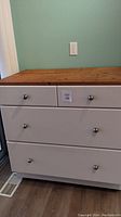 Front view showing white base with two small top drawers, two lower drawers and wood top