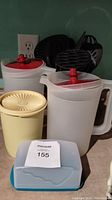 Photo showing two white plastic pitchers with red lids, black plastic utensils in white holder, yellow canister, and blue butter dish.