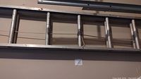 Full view of aluminum extension ladder in contracted state hung horizontally on wall.