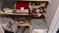 Photo showing shelves with folded blankets, comforters in plastic bags, floral hook rug, and pillow cases.