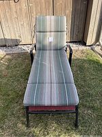 Lounge chair with green, white, and pink striped cushion pad on the grass outside a wooden shed.