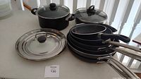 Group photo of six cooking pans, cooking pot with glass lid, egg poacher pan with lid, and two lids.