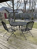 45-degree view of round metal patio table with four chairs on wooden deck